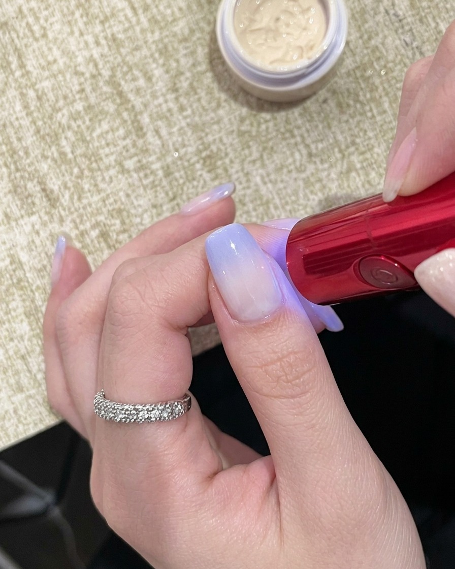 Une main positionnée sous une lampe UV compacte portative, les ongles visibles en dessous.