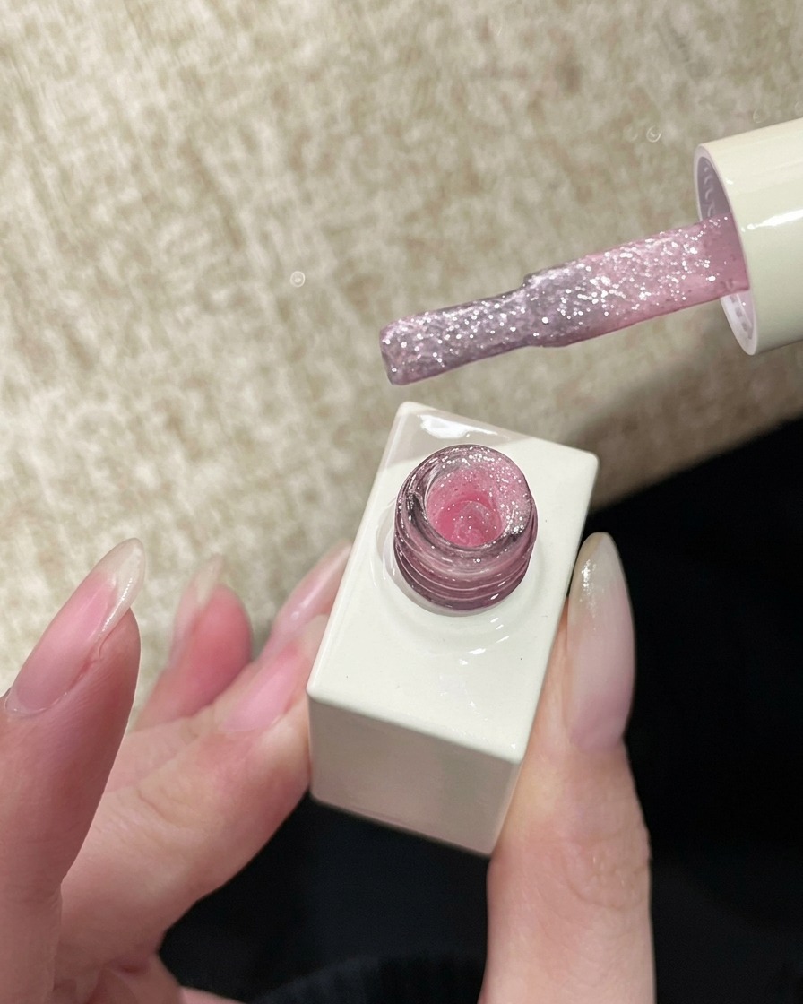 Un pinceau à vernis tenant un gel pailleté rose translucide, prêt à être appliqué sur longle.