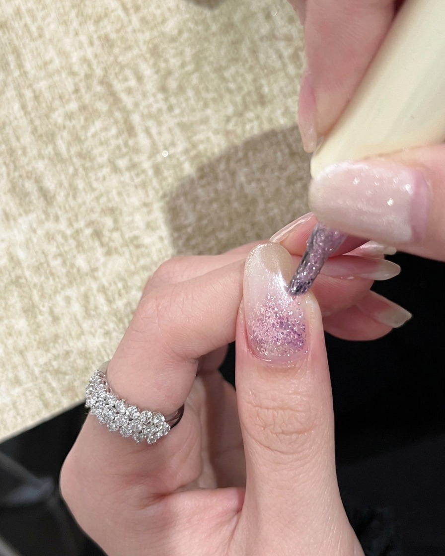 Une main sous une lampe UV portative avec des ongles montrant un effet dégradé rose clair.