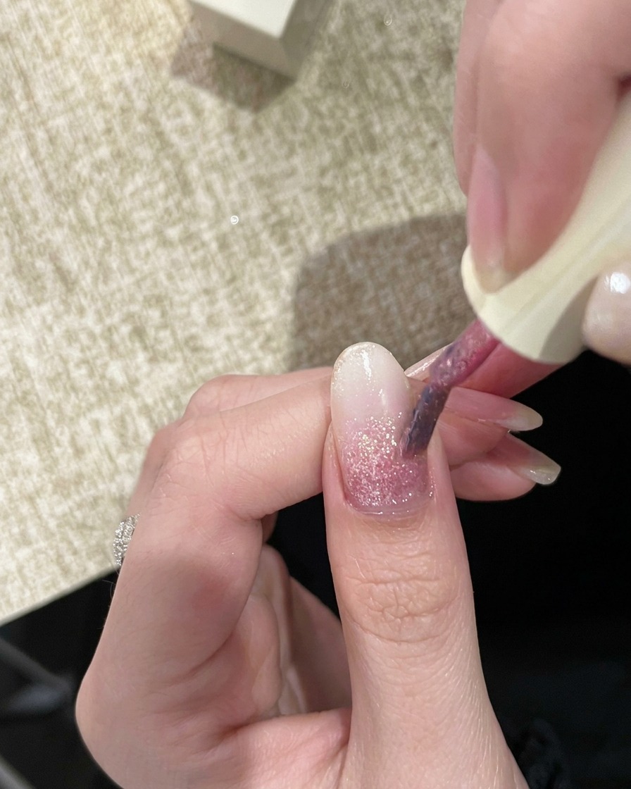 Un pinceau à ongles appliquant un deuxième gel pailleté rose légèrement plus pigmenté sur longle.