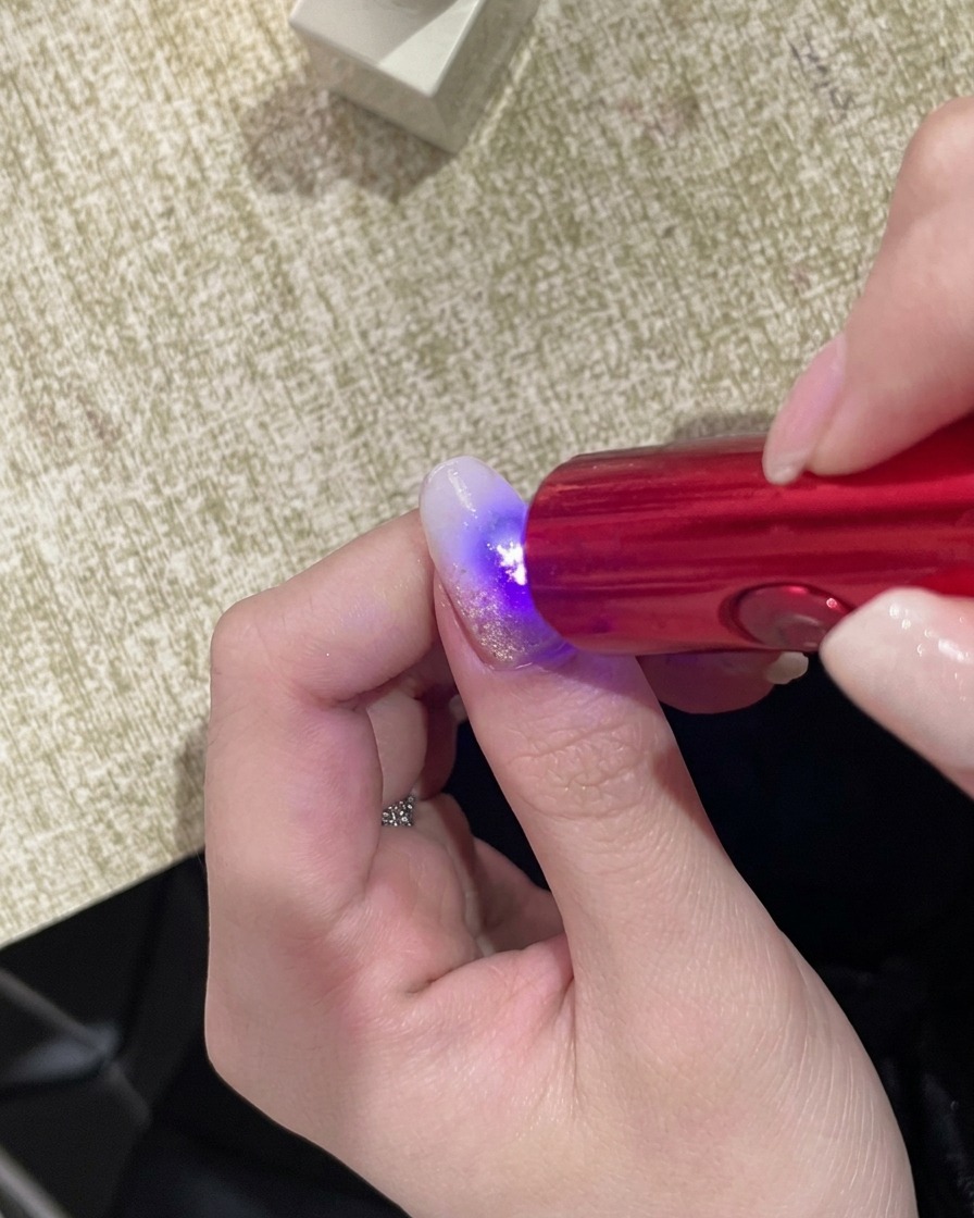 Une main positionnée sous une lampe UV portative compacte, avec la surface de longle brillant sous la lumière.