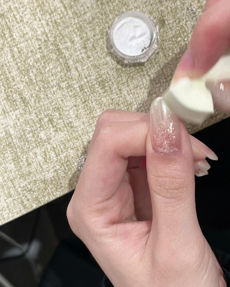 Un applicateur en mousse tapotant de la poudre chrome dorée sur le bord libre dun ongle.