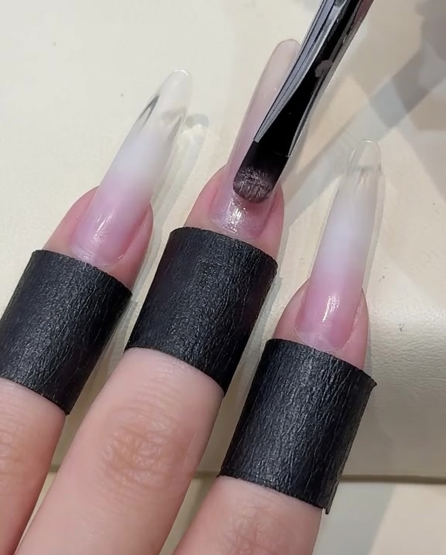 Pinceau appliquant une couche de gel cat-eye nude clair sur longle.