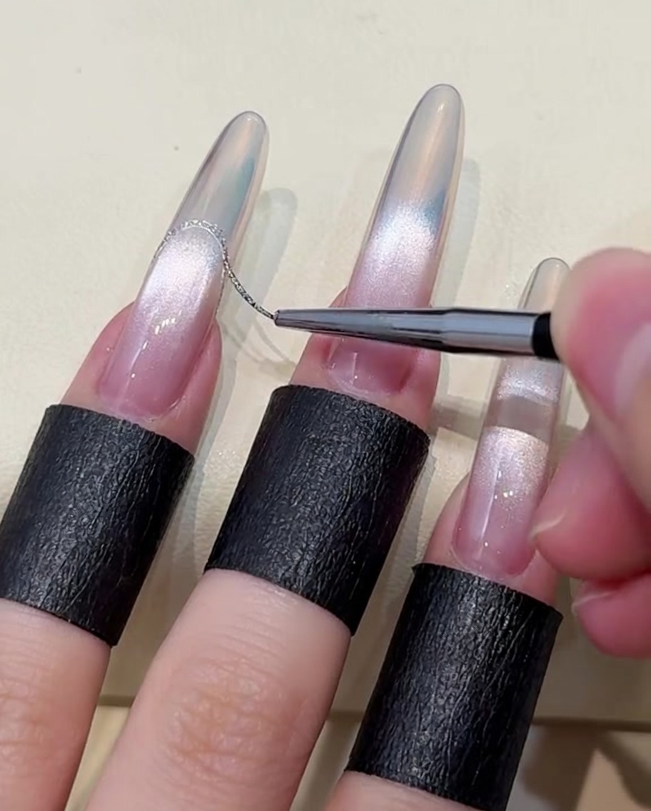 Gros plan dun pinceau liner appliquant une ligne argentée pour créer une french sur un ongle aurora.