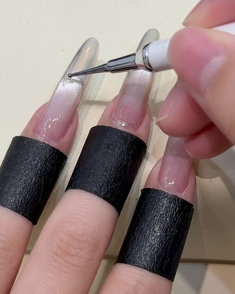 Gros plan dun outil de dotting déposant des points de gel adhésif sur longle.