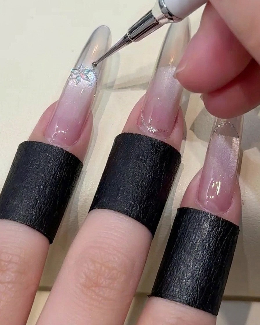 Pinces déposant un cristal flocon et des petites billes dacier sur longle.