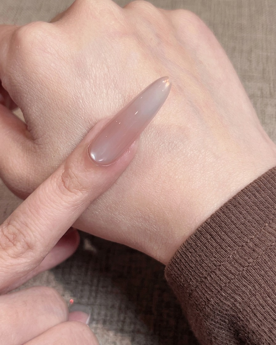Gros plan dun pinceau appliquant une fine couche de gel nude sur un ongle préparé.
