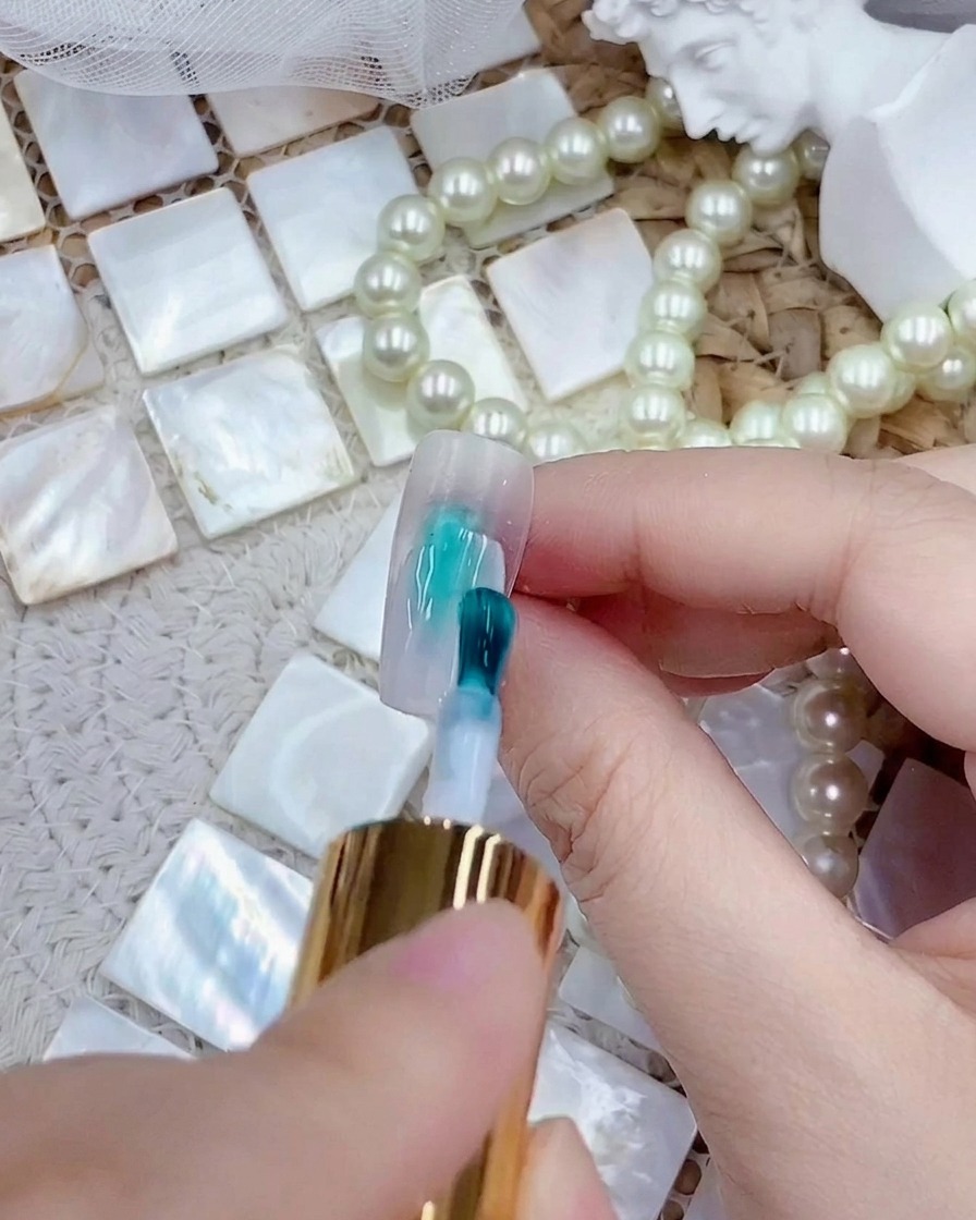 Un pinceau appliquant une couche de vernis gel blanc laiteux sur une capsule press-on transparente.