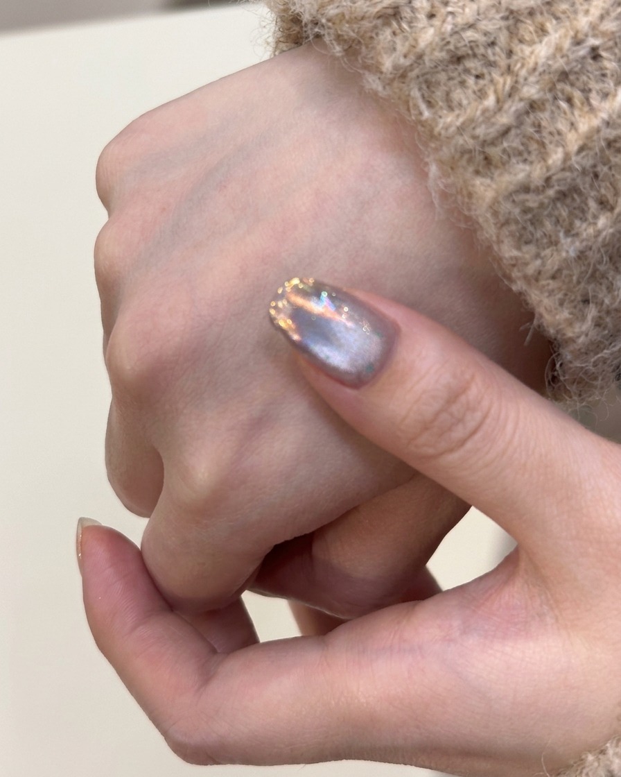 Un pinceau appliquant une couche de vernis gel magnétique argenté sur un ongle naturel.
