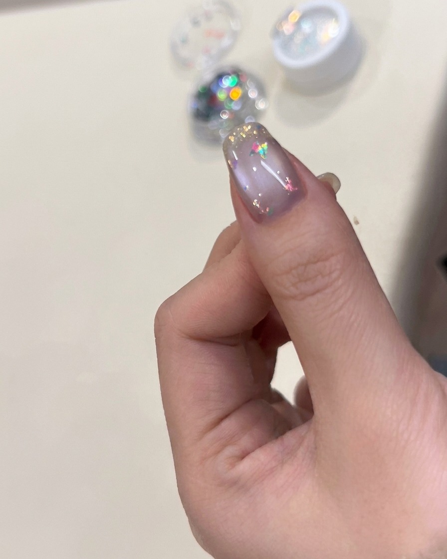 Un pinceau appliquant une finition brillante sur un ongle décoré de flocons et dun papillon.