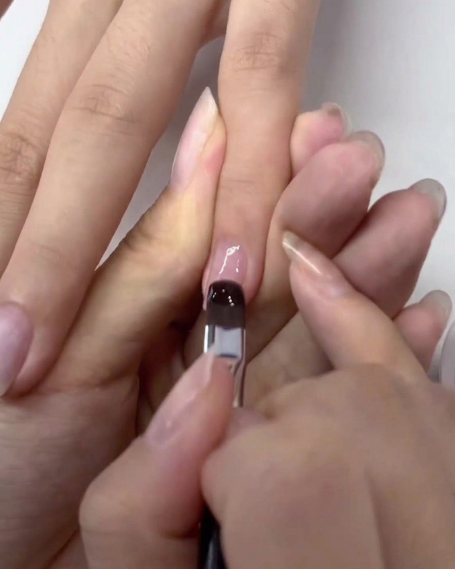 Un pinceau appliquant une couche fine de base gel transparente sur un ongle préparé.