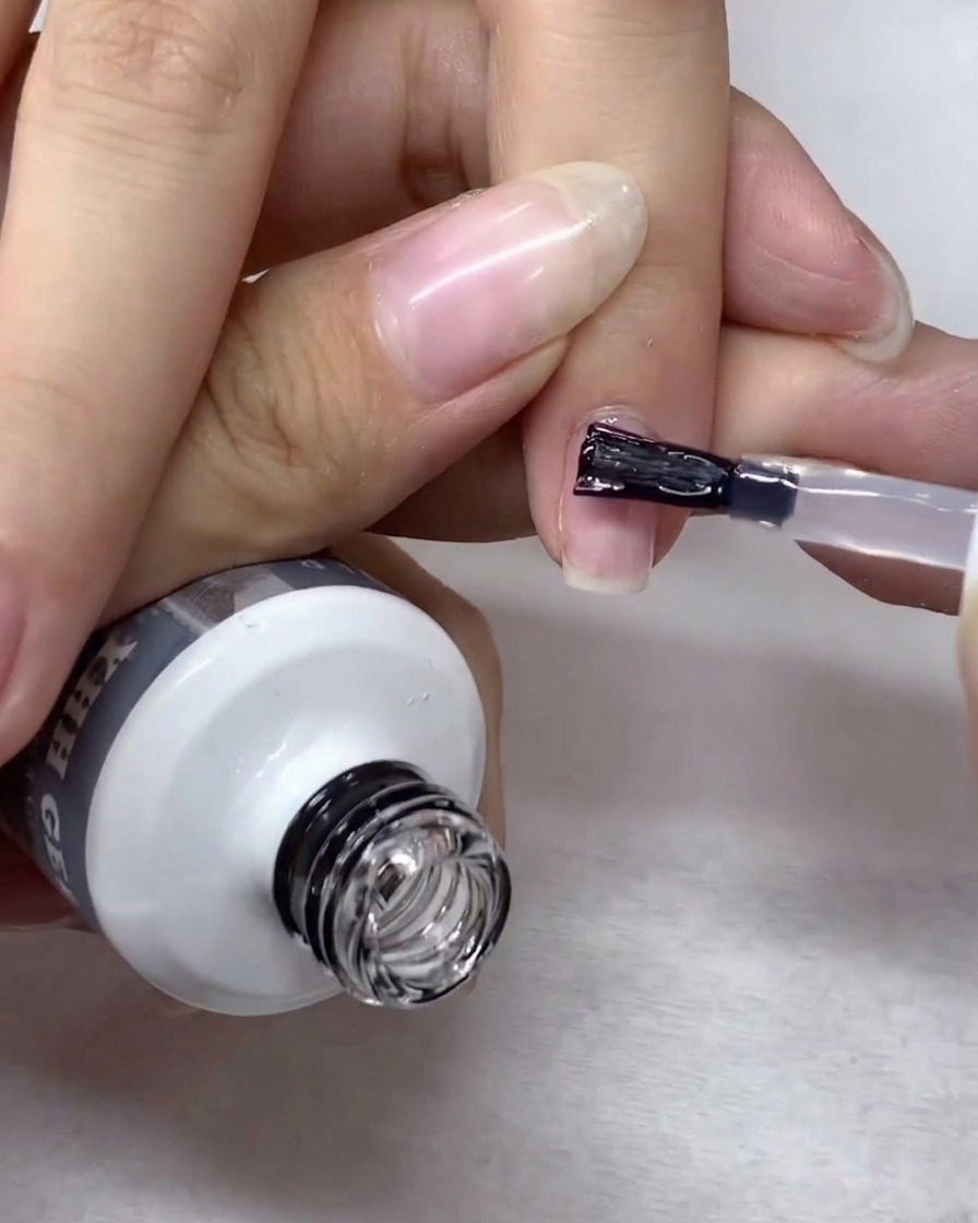 Un pinceau à nail art guidant doucement le gel de renforcement sur toute la surface de longle.
