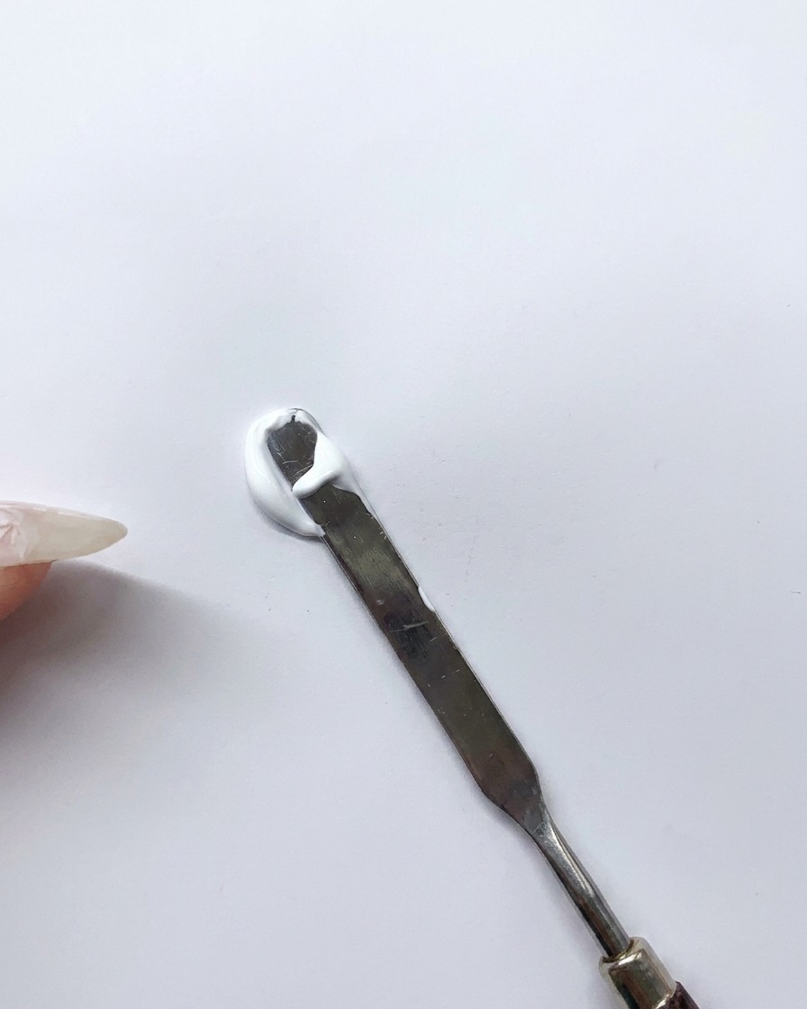 Une spatule mélangeant du gel blanc et bleu sur une palette pour créer une teinte bleu clair.