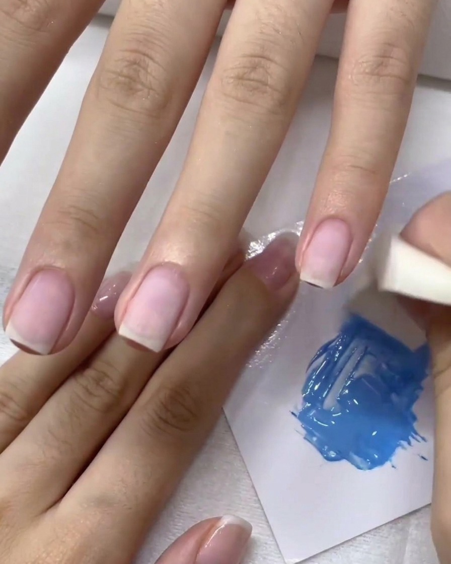 Une éponge à maquillage tapotant du gel bleu sur longle pour créer un effet ombré.
