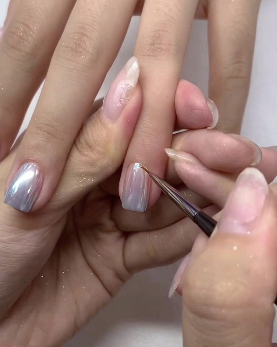 Un pinceau appliquant soigneusement la dernière couche de top coat sur les ongles chromés.