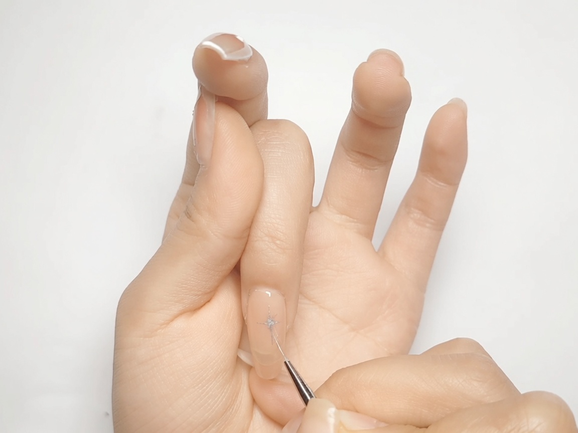 Un pinceau nail art remplissant les coins en forme de losange dune étoile argentée sur un ongle nude.