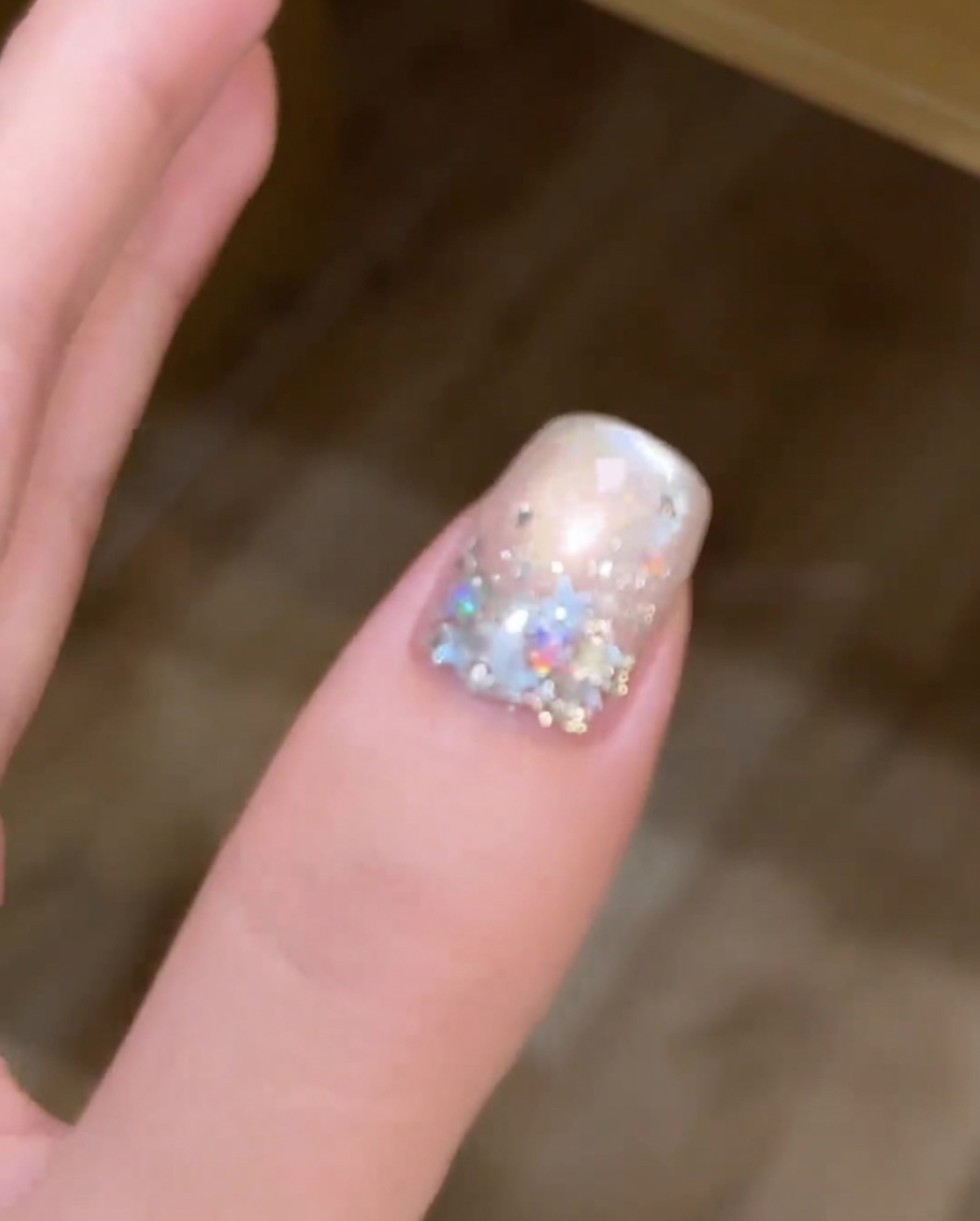 Un pinceau appliquant une couche de vernis gel magnétique argenté sur un ongle peint en blanc.