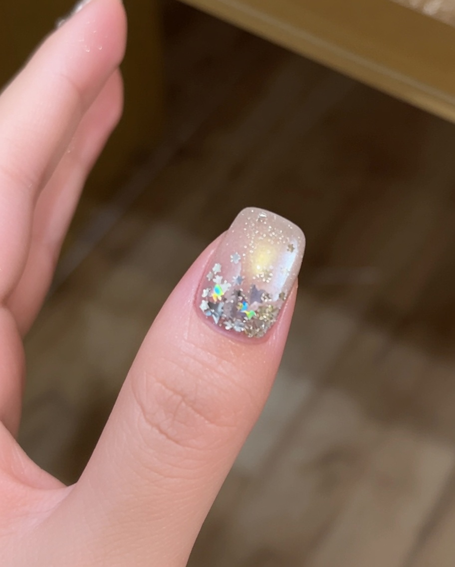 Gros plan dun doigt avec de grandes paillettes étoiles argentées placées sur une surface dongle enduite de gel avec un pinceau fin.