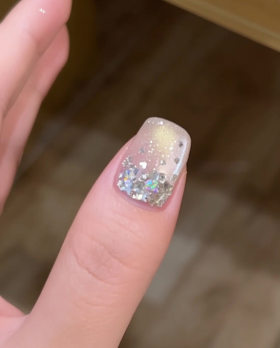 Une fine couche de gel de construction transparent appliquée au pinceau sur un ongle décoré de paillettes étoiles.