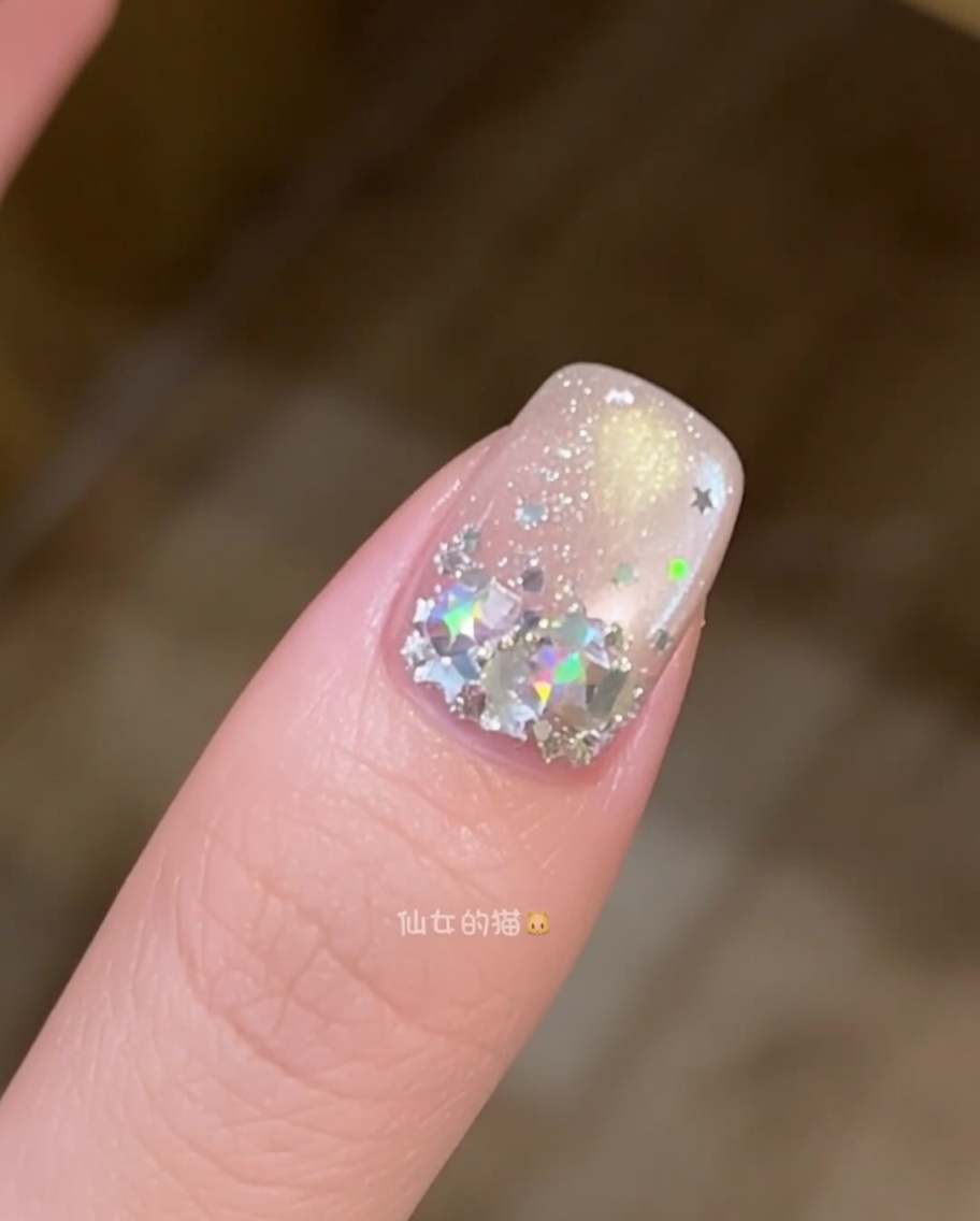Gros plan dun pinceau à ongle lissant une couche de gel de construction transparent sur un ongle décoré de paillettes étoiles.