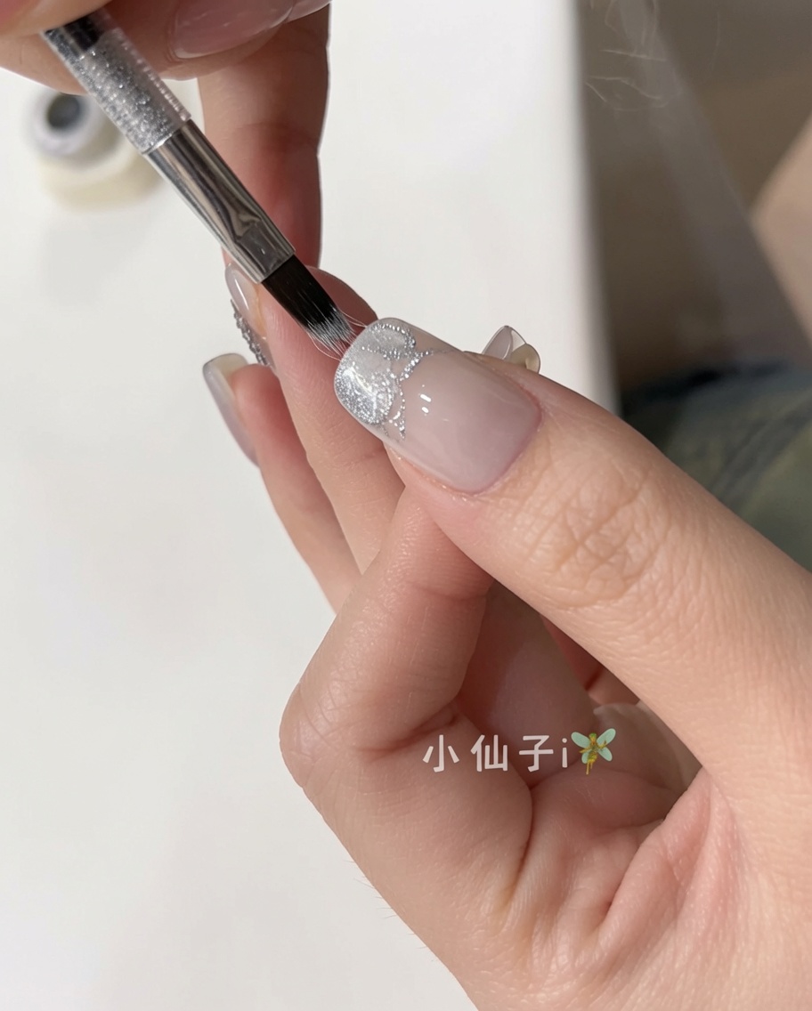 Un pinceau appliquant un vernis gel cat eye argenté scintillant sur un ongle naturel préparé.