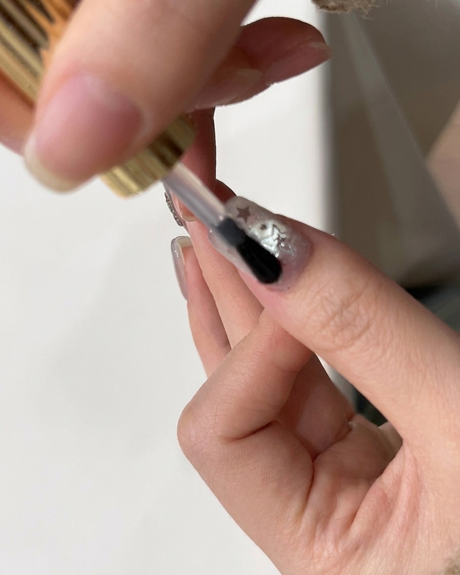 Un pinceau appliquant un top coat brillant final sur un ongle décoré de paillettes.