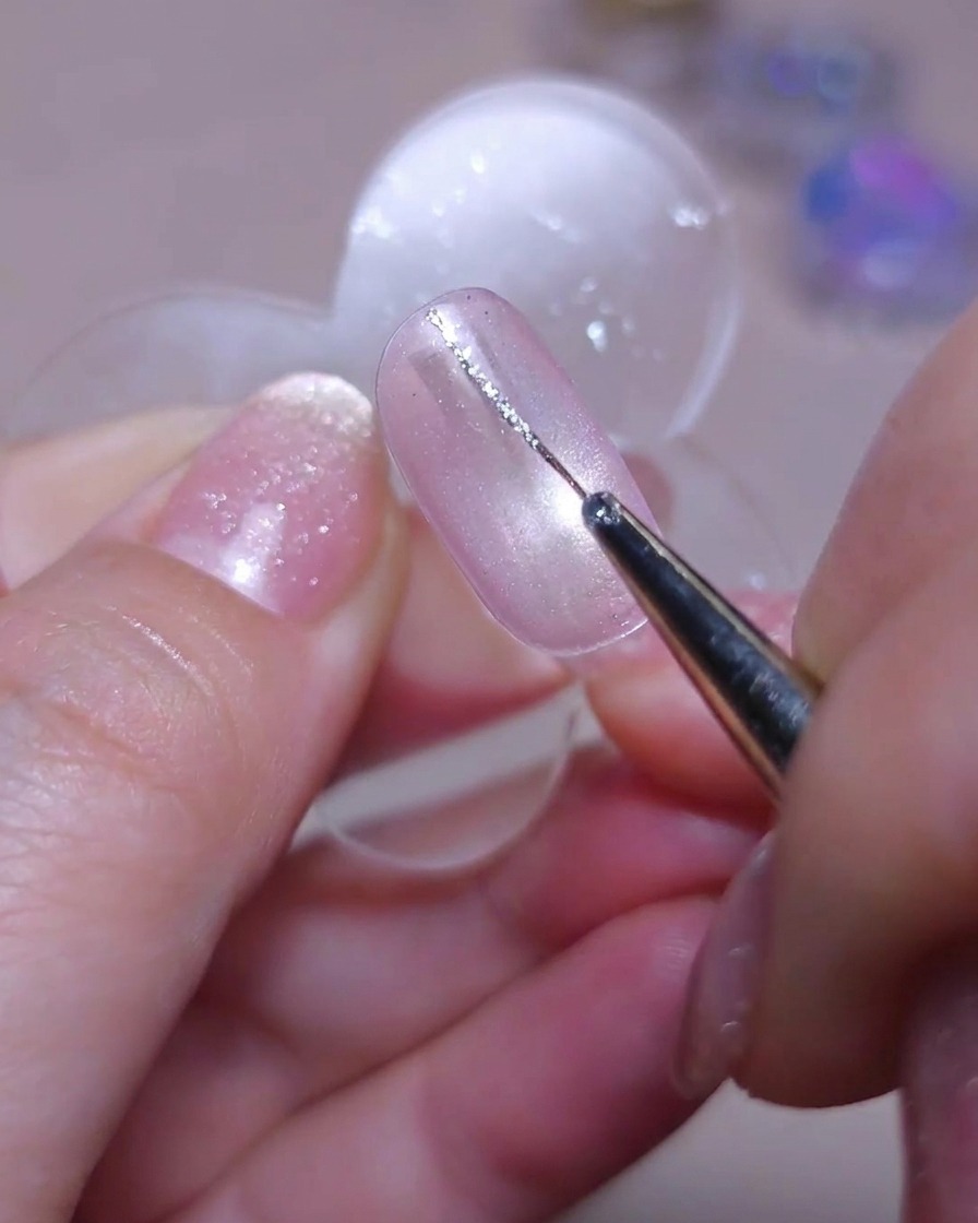Un pinceau liner fin dessinant une délicate ligne verticale avec du gel pailleté argenté sur le côté gauche dun ongle cat-eye.