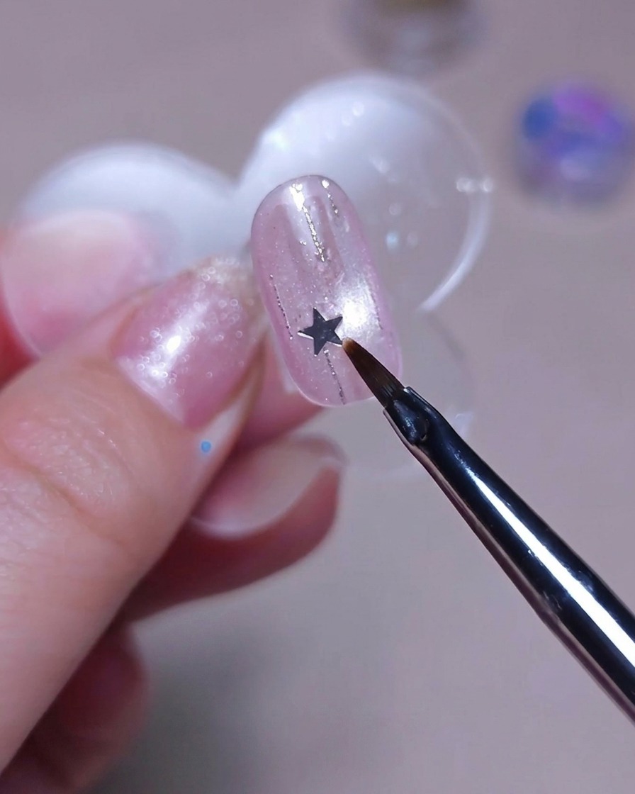 Un pinceau fin plaçant un petit sequin étoile argenté sur un ongle.