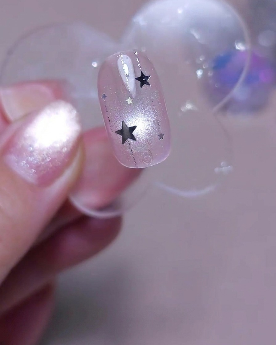 Un pinceau appliquant une couche finale de top coat transparent brillant sur un ongle décoré de lignes et de sequins étoiles argentés.