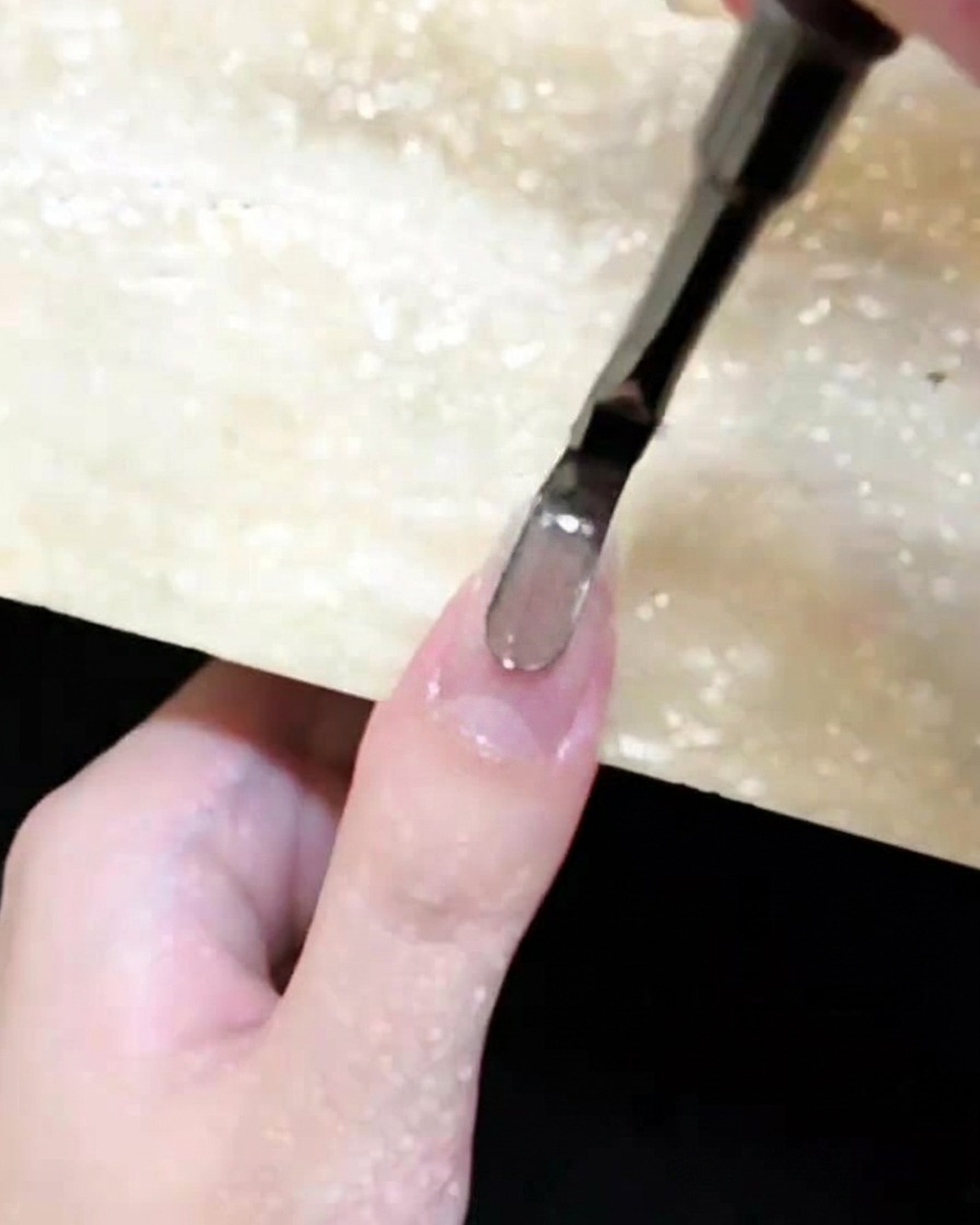 Gros plan dun pinceau appliquant du gel œil de chat marron sur un ongle naturel.