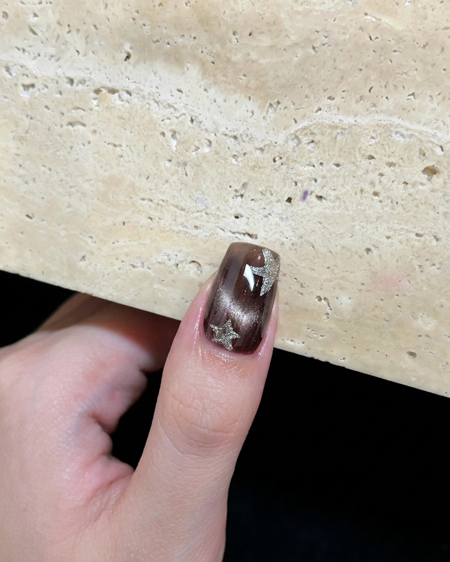 Un ongle œil de chat marron décoré de deux étoiles en argent platine peintes à la main.