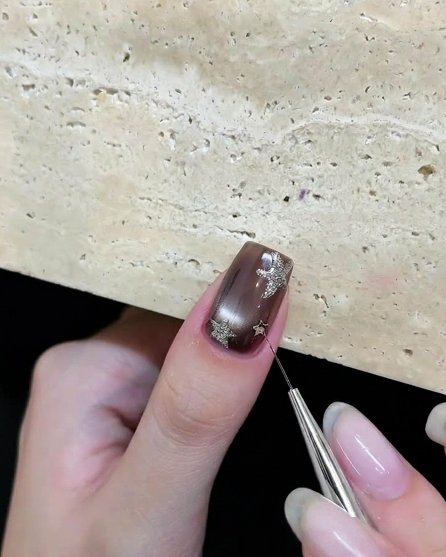 Un outil plaçant des paillettes argentées en forme détoile sur un ongle en gel marron.