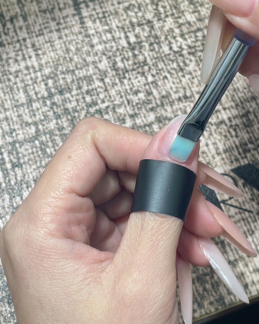Gros plan sur un pinceau à ongles appliquant un vernis gel nude transparent sur un ongle naturel nu et préparé.