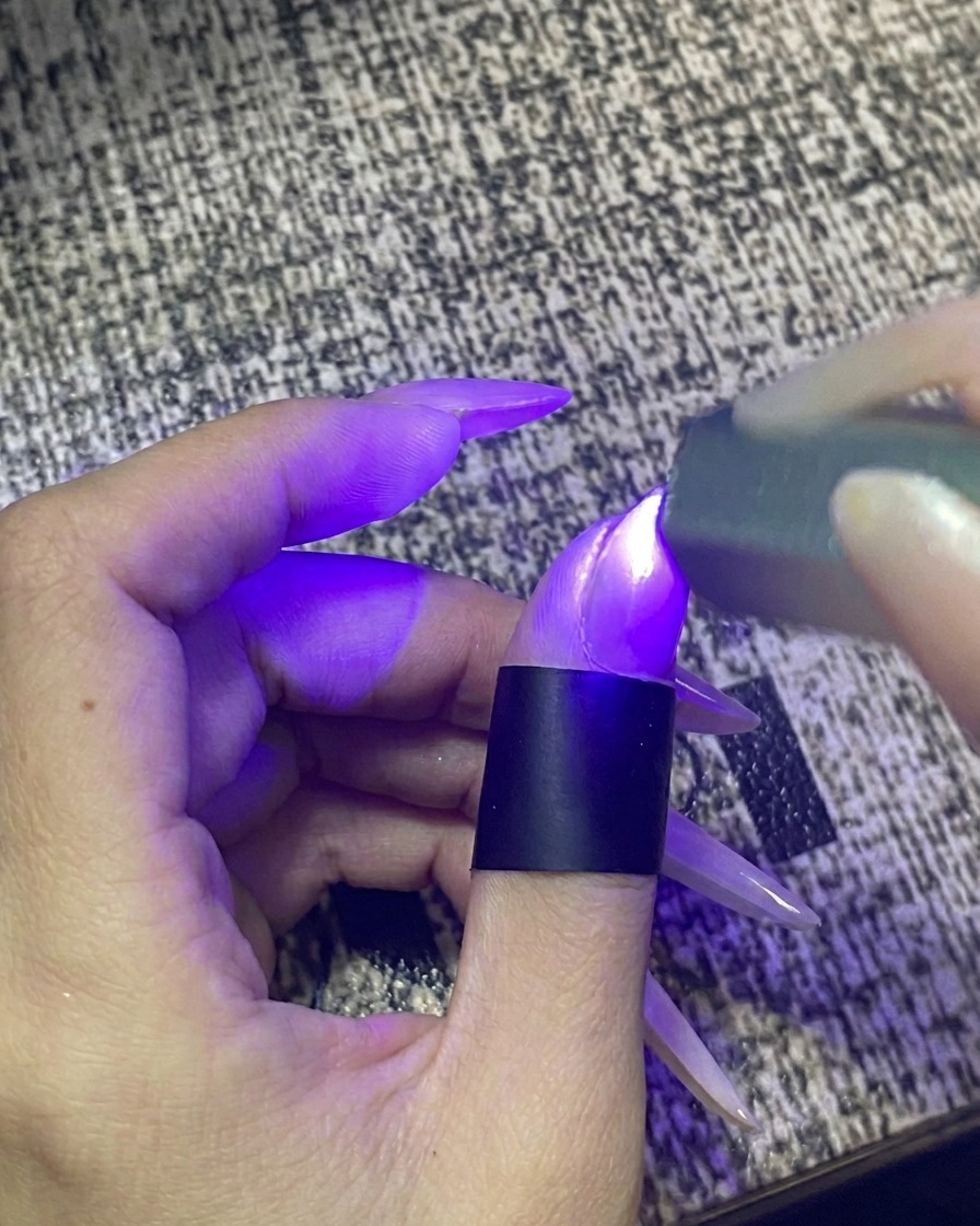 Un doigt placé à lintérieur dune lampe à ongles portable UV/LED avec la lumière activée.