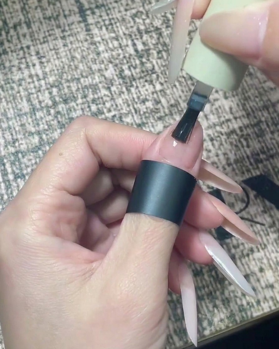 Un pinceau à ongles appliquant précisément une couche de finition transparente sur la moitié supérieure dun ongle peint en nude.
