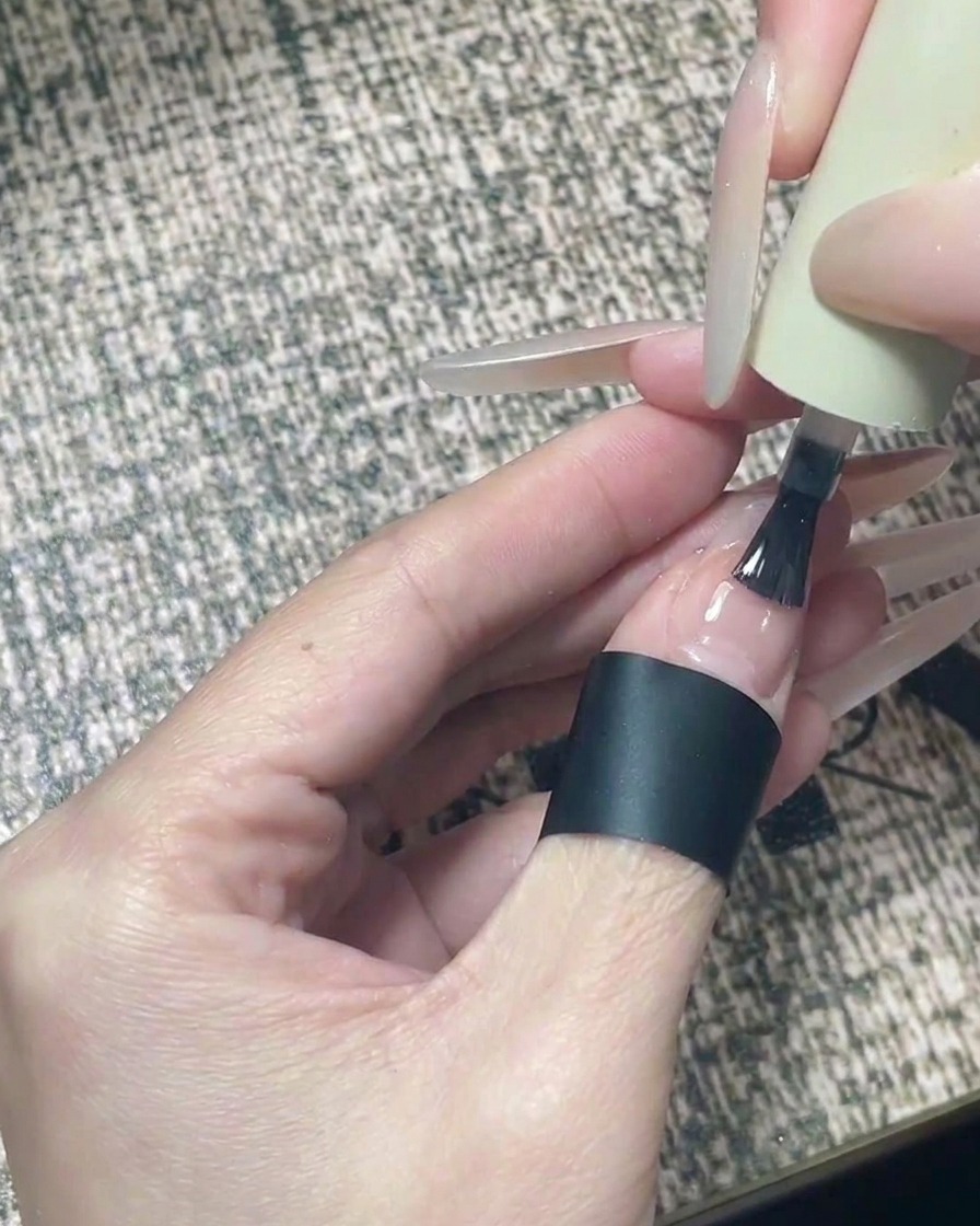 Un pinceau appliquant un top coat brillant transparent sur un design dongle fini avec des étoiles noires.