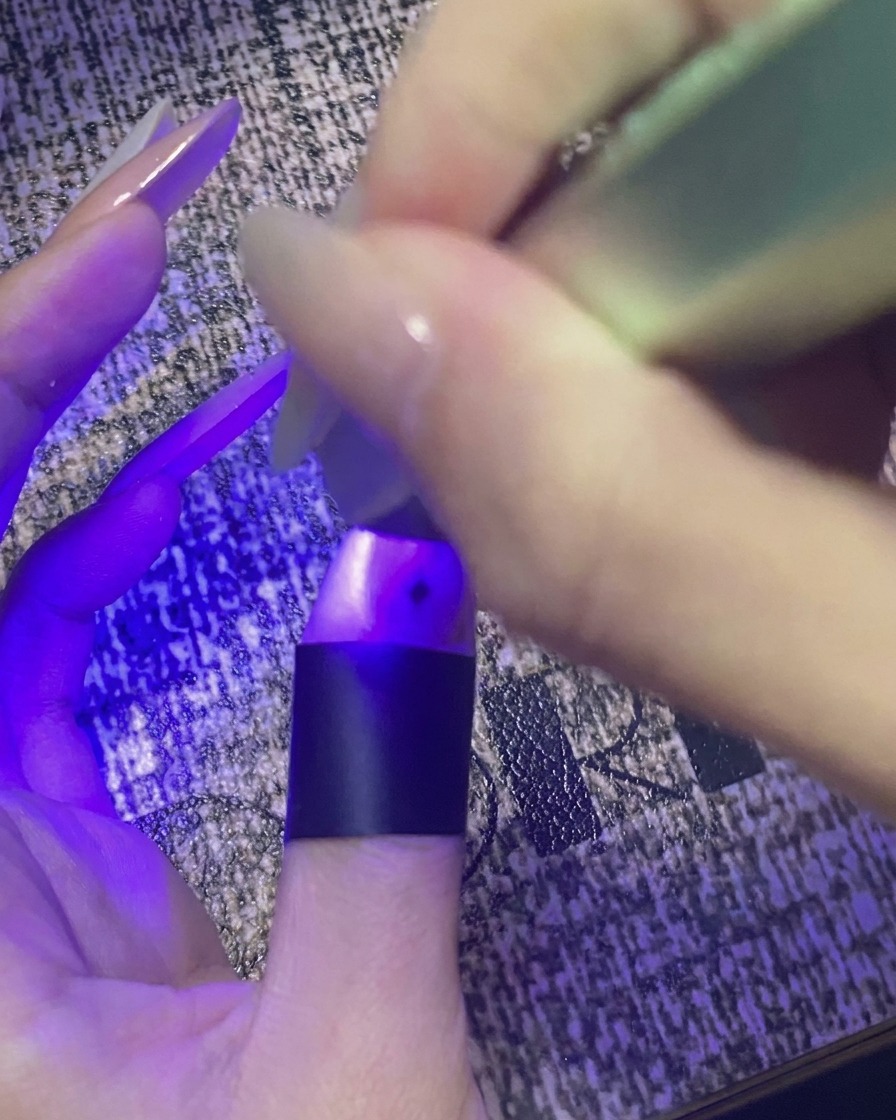 Un pouce avec un nail art étoile catalysant sous une mini lampe UV/LED violette.