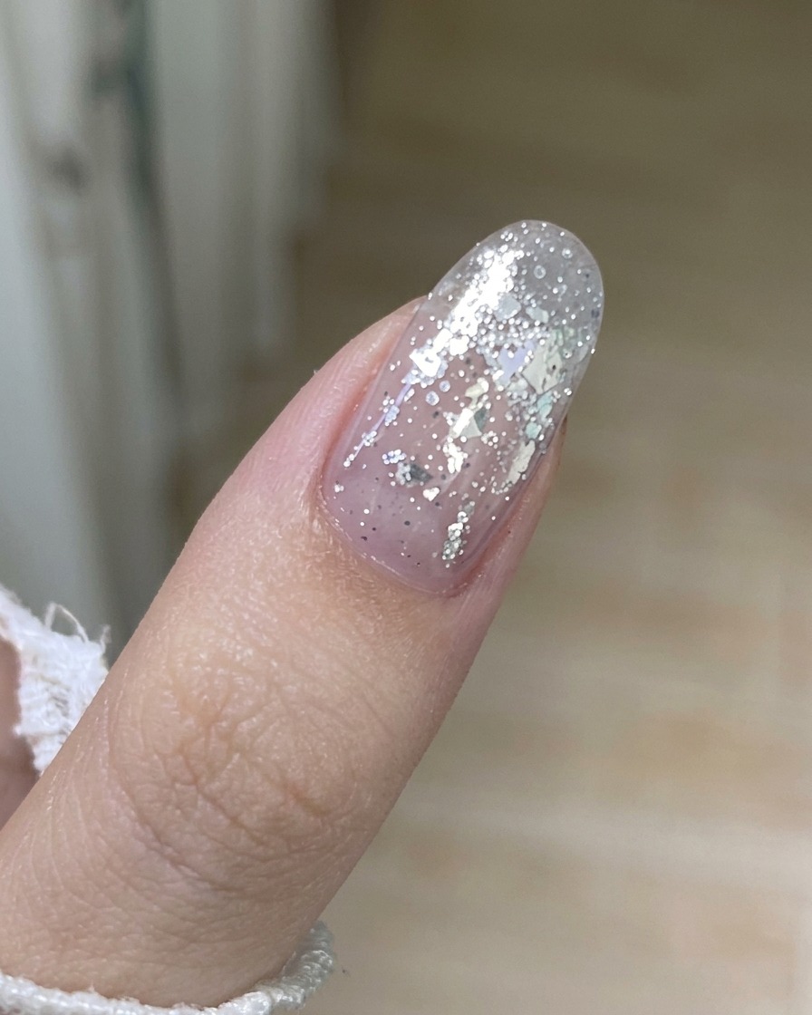 Gros plan sur un outil en métal soulevant délicatement le bord dune ancienne couche de vernis semi-permanent sur un ongle.