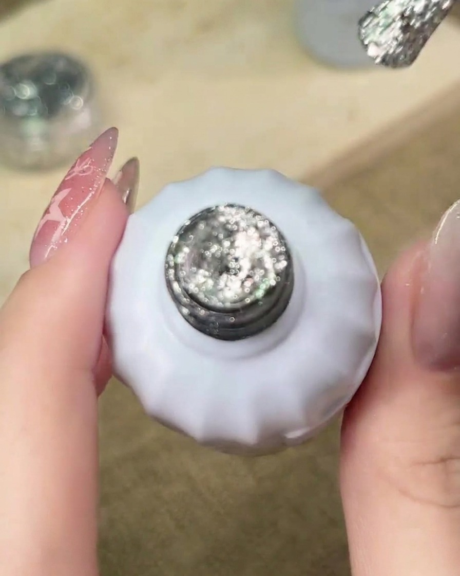 Un pinceau appliquant du gel à paillettes argentées sur le bord libre de longle, amorçant le processus de dégradé.