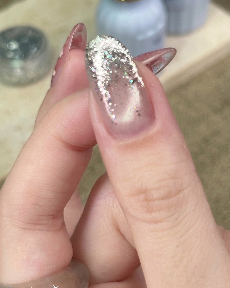 Gros plan sur un outil plaçant une petite étoile métallique sur un ongle au dégradé de paillettes argentées.