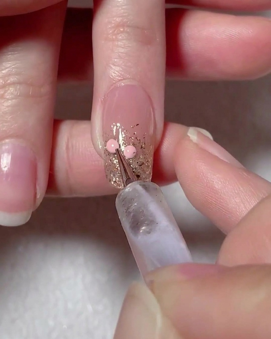 Un outil de dotting plaçant deux points de gel rose sur la surface de longle pour dessiner un cœur.