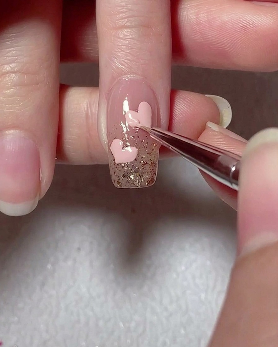 Un pinceau liner affinant les contours dun cœur en gel rose sur un ongle accentué de paillettes.