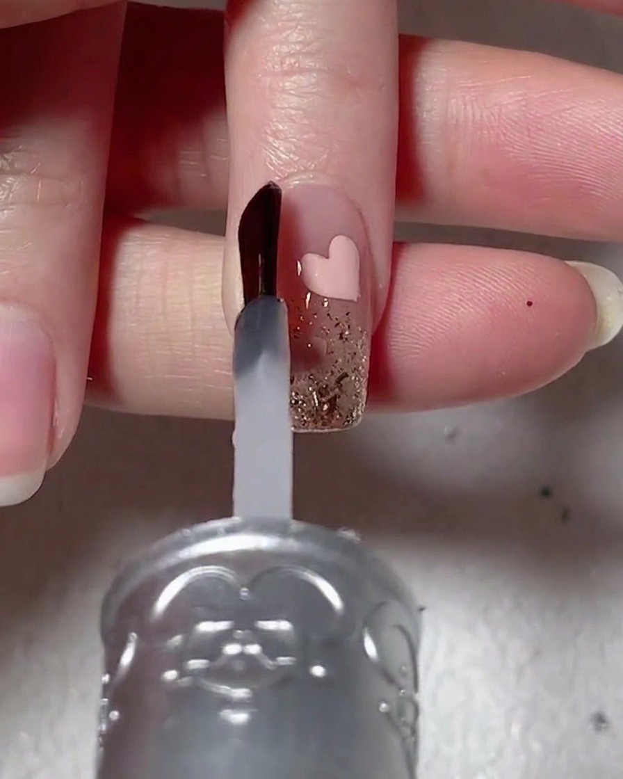 Un pinceau à ongles appliquant un gel de renforcement transparent et visqueux sur un ongle décoré.