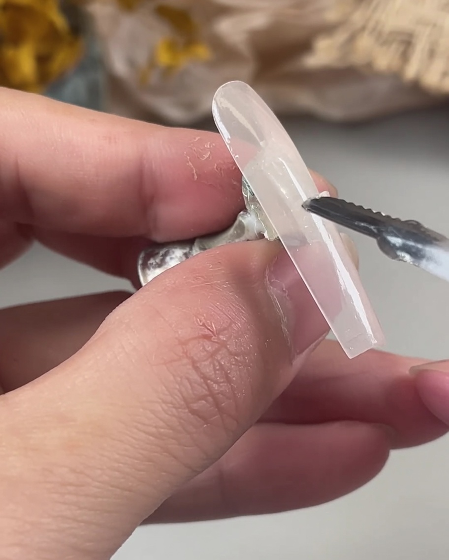 Une main utilisant un outil pour placer soigneusement des flocons de paillettes holographiques et irisées sur le gel humide et non polymérisé dune capsule.