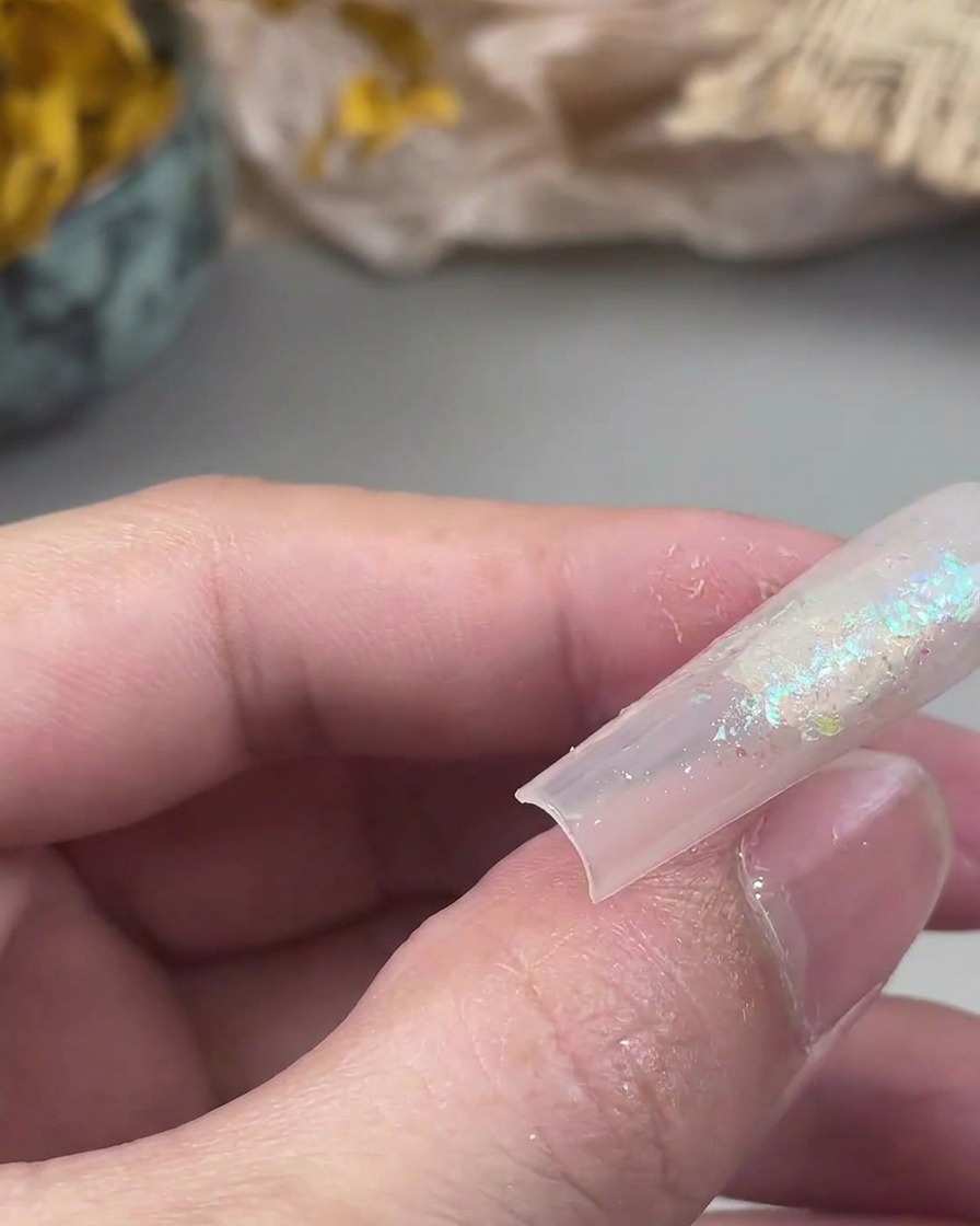 Un petit pinceau plat pressant des particules de paillettes libres sur une surface de gel collante sur un ongle.