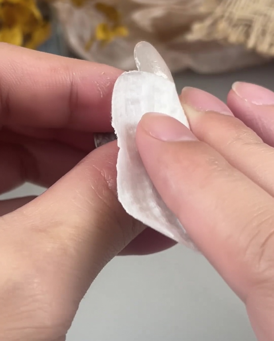 Une main utilisant un coton non pelucheux pour nettoyer la surface dun ongle en gel polymérisé.
