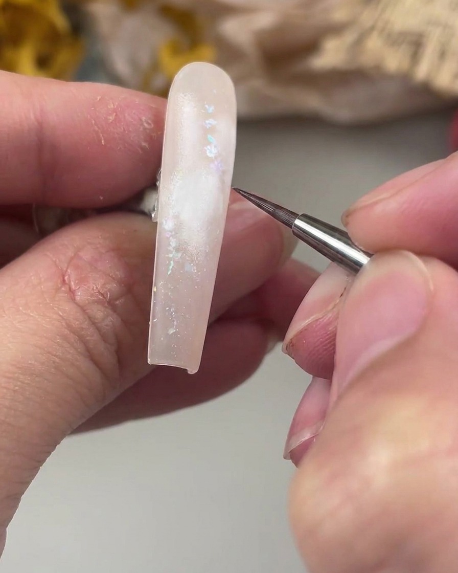 Un pinceau liner fin posé au-dessus de la zone peinte en blanc sur longle, prêt à peindre le centre délicat de la rose à laquarelle.