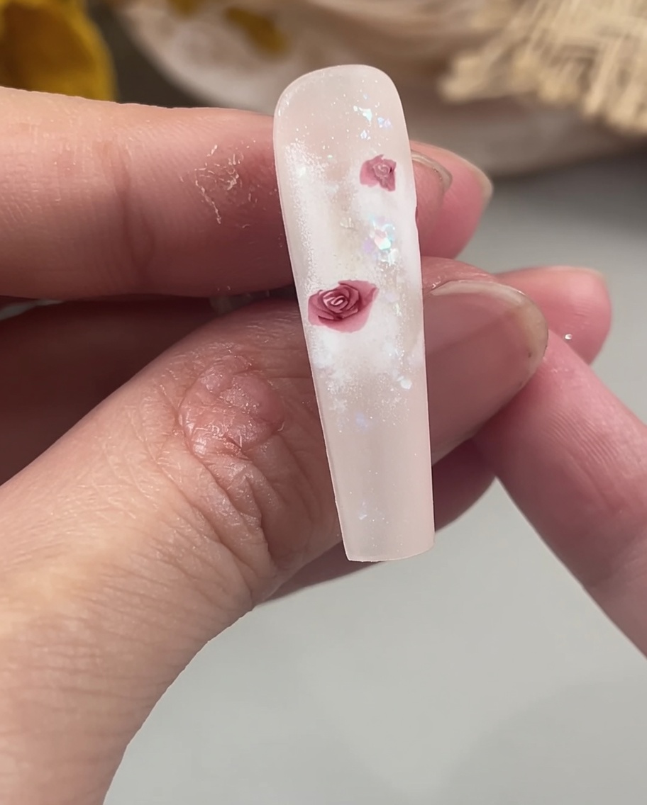 Un pinceau de détail remplissant le centre des pétales de rose sur un ongle pour créer une forme florale solide et définie.