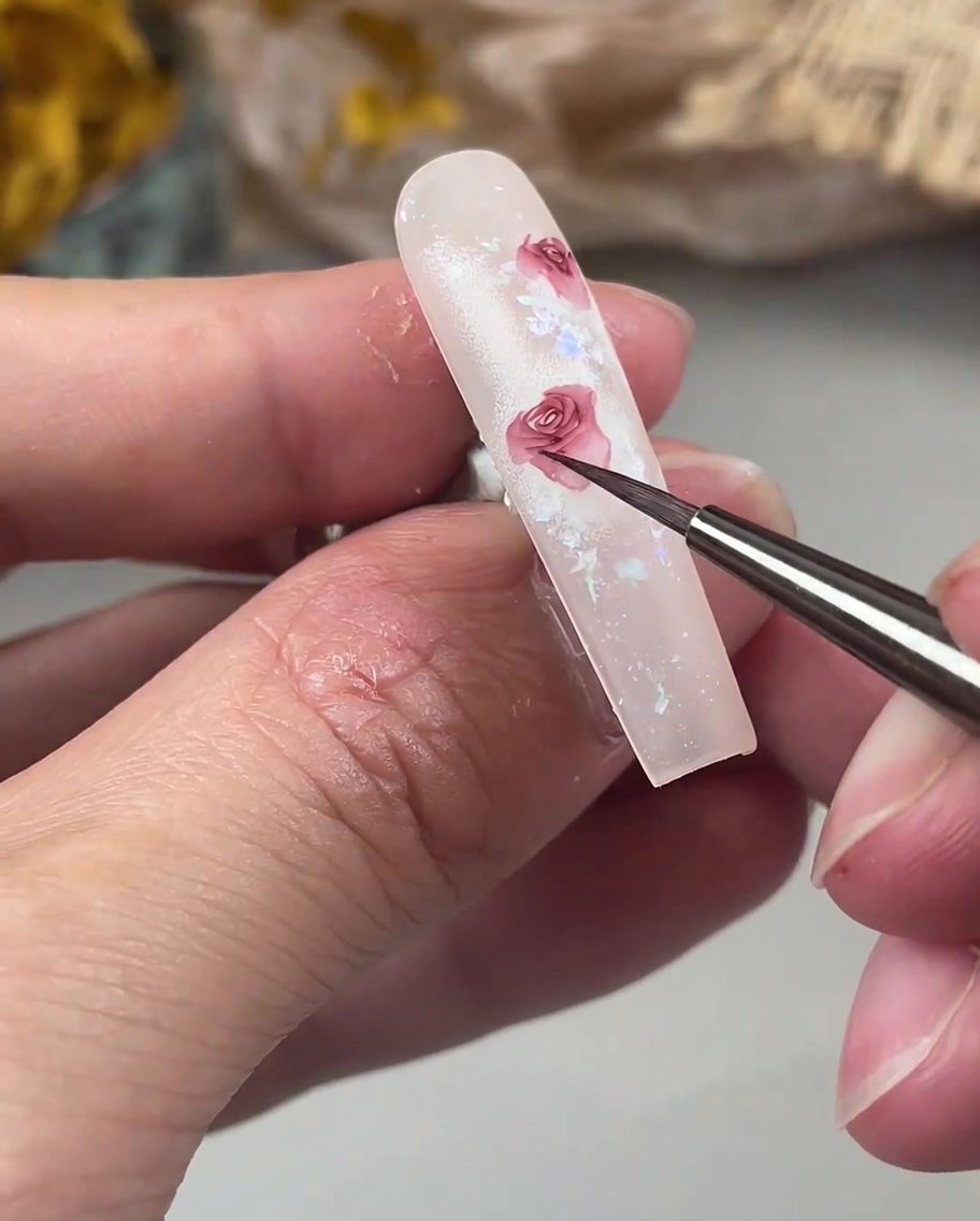 Un pinceau de détail ajoutant de délicats pétales sincurvant vers lextérieur sur le bord dun motif de rose sur un ongle.