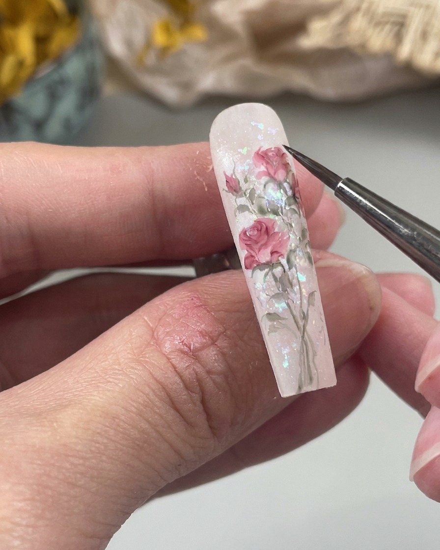 Une vue en gros plan dun pinceau fin pour nail art peignant une petite forme de goutte deau rose pâle sur la surface dun ongle dans le cadre dun motif floral.